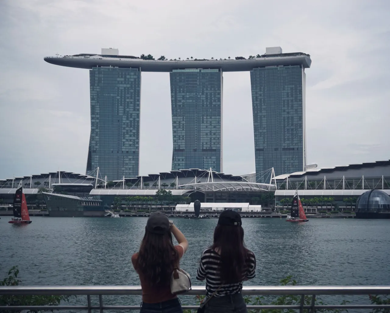 Two women admire Marina Bay Sands, Singapore's iconic architectural landmark, from a waterfront viewpoint.