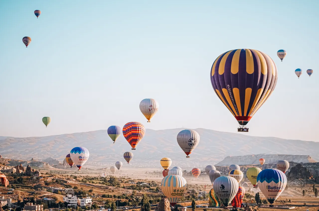 A scenic view of hot air balloons floating over Cappadocia, Türkiye at sunrise.