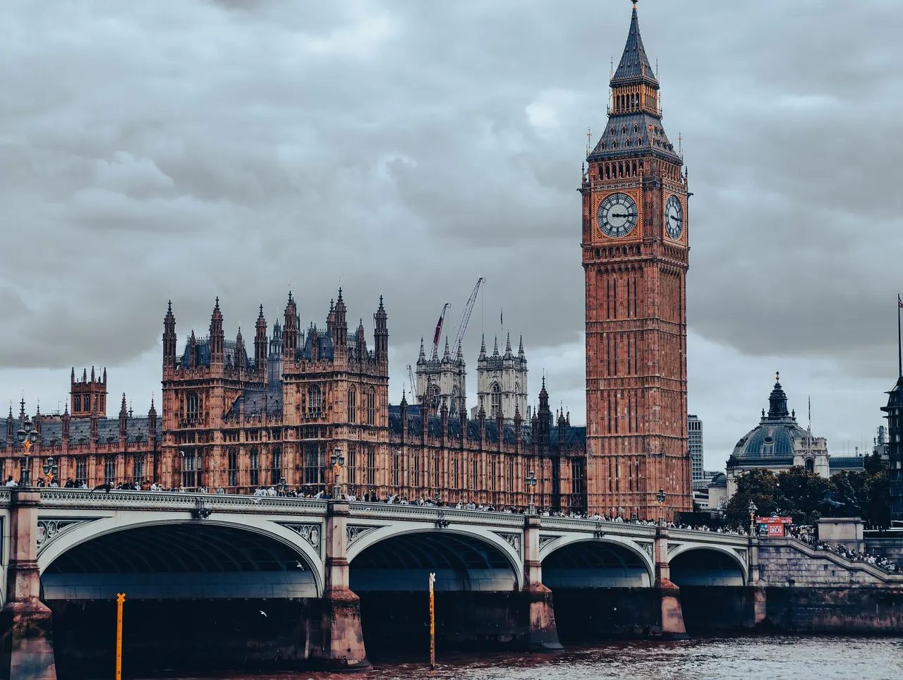 Dramatic view of Big Ben and Westminster Bridge against cloudy skies in London.